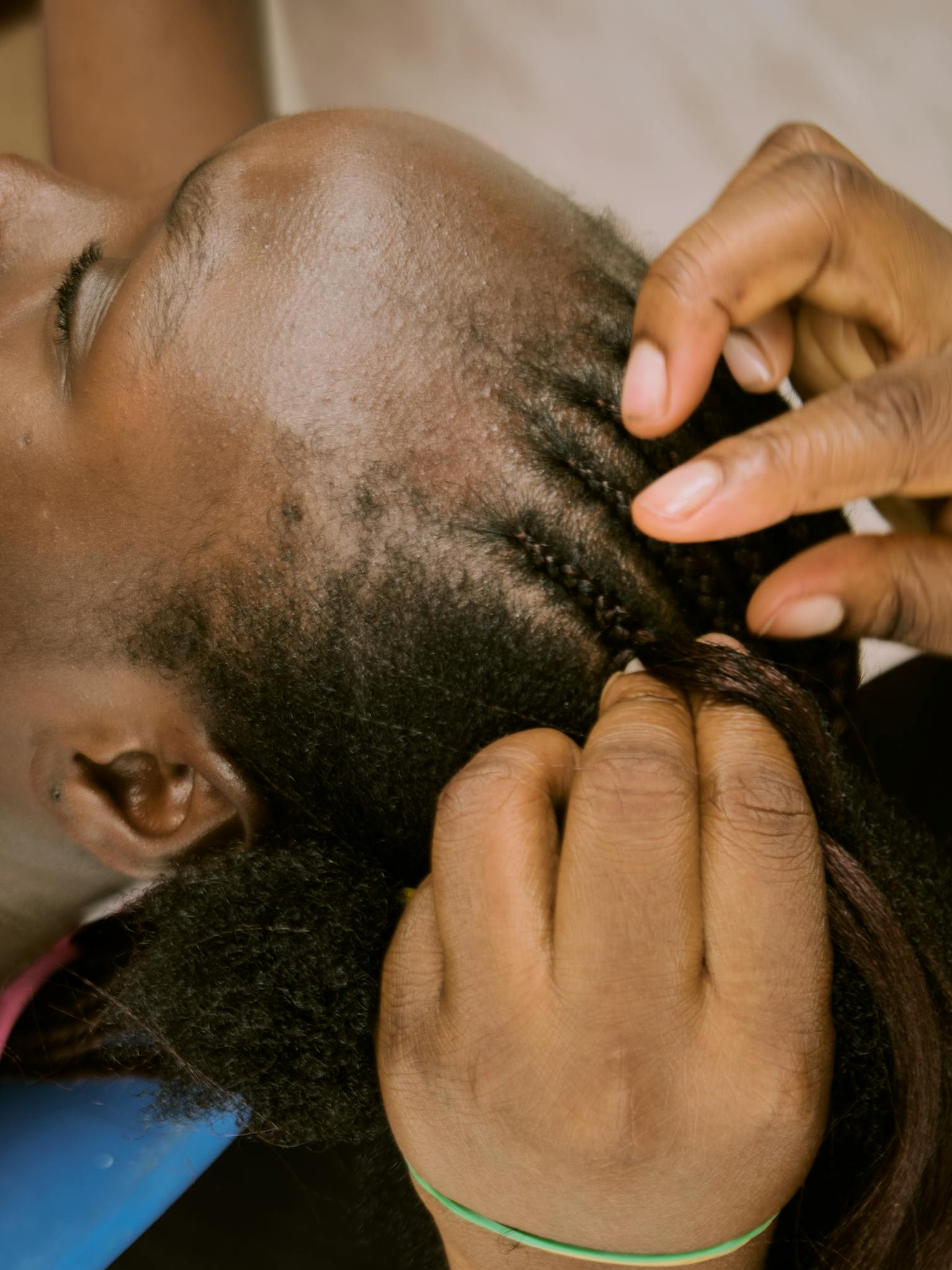 Home A detailed close-up shot of an African woman having her hair braided by skilled hands.