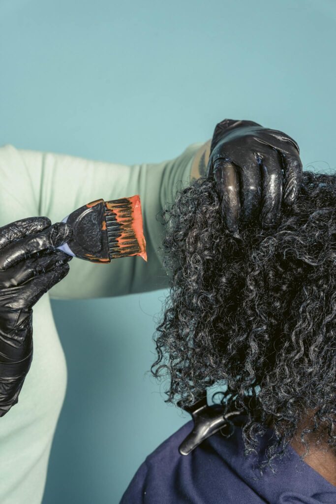 Close-up of hairstylist applying hair dye on client with curly hair in salon.